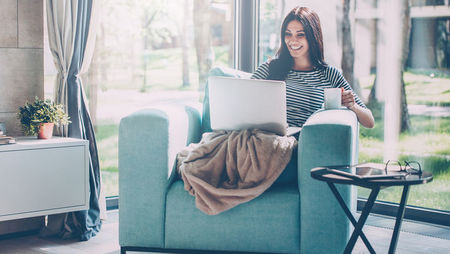 Young woman sitting in armchair and working on laptop from home