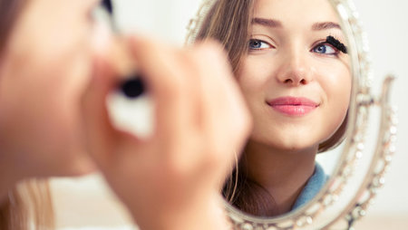 Woman applying makeup in front of mirror