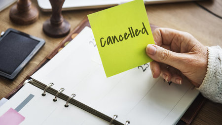 Close-up of a woman's hand holding a sticky note that says 'Cancelled'