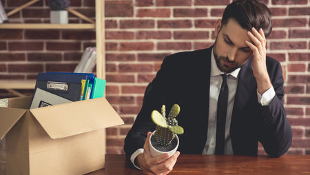 A young, sad businessman holding a cactus and packing his belongings in a cardboard box