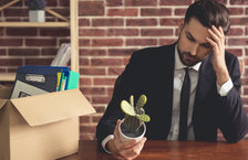 A young, sad businessman holding a cactus and packing his belongings in a cardboard box