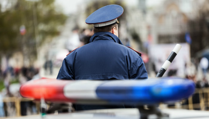A male police officer holding a baton and standing in front of a police car