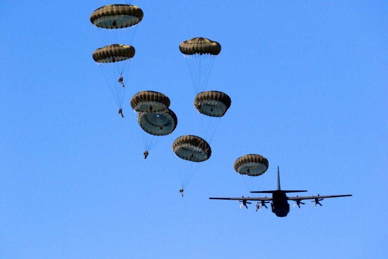 Seven paratroopers with open parachutes in front of a military plane