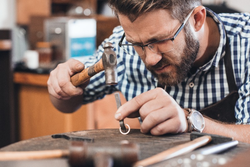 Jeweler holding a hammer and working on a ring